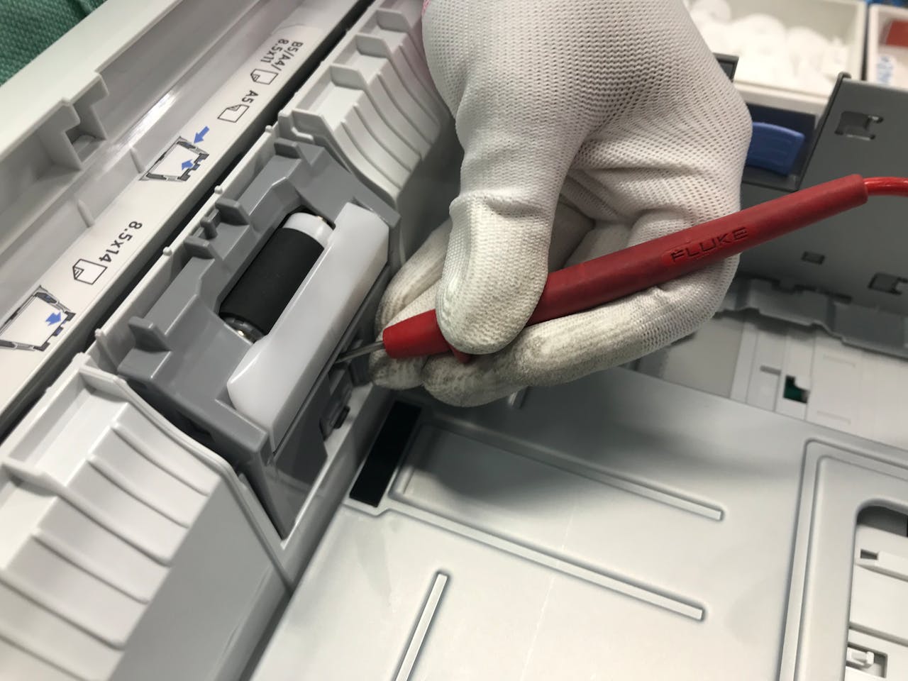 A gloved hand fixes a printer using a red precision tool, showcasing maintenance skills.